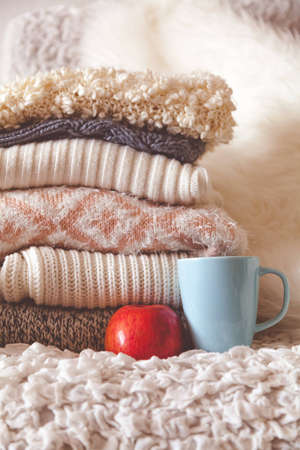 Stack of cozy knitted clothes with red apple and cup of teaの写真素材