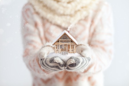 Young woman in mittens holding snow in her hands with a log house. Unusual christmas conceptの写真素材