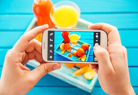 Man taking picture of vintage tray with fruits on her smartphone. Top viewの写真素材