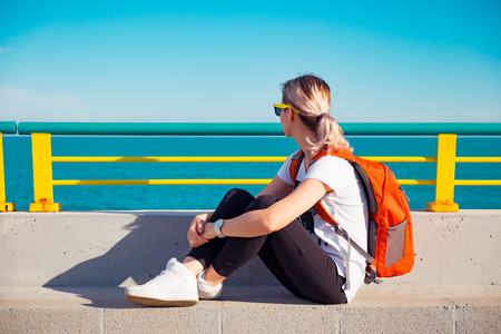 Young traveller woman with backpack sitting on a pier  and looking to the seaの写真素材