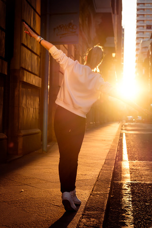 Young stylish woman walking by the road on the street at sunset.