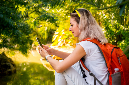 Pretty woman is using smartphone resting at the river in a forestの写真素材