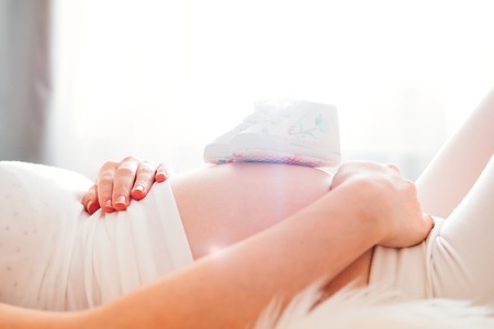 Cute small shoes for the baby on the pregnant womans bellyの写真素材