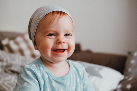 Cute little happy laughing baby girl plays sitting on a bed in a room. Happy family having fun.の写真素材