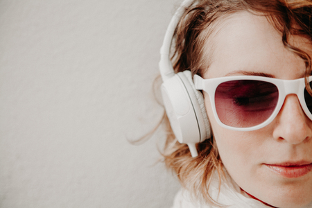 Beautiful young woman in a sunglasses and headphones listening to music standing at the wall. Casual style concept.の写真素材