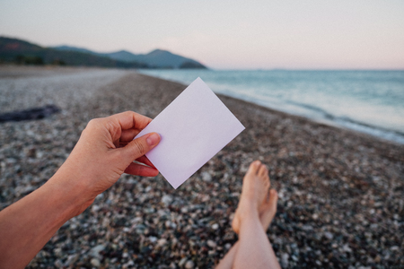 Empty paper note in hand on amazing landscape background. Travel and Vacation concept. White piece of paper with no textの写真素材