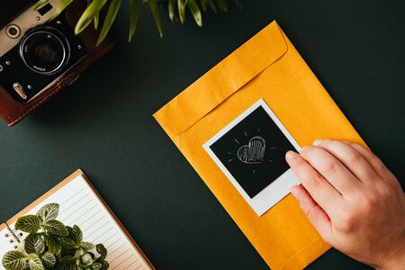 Top view of flat lay of hand lies next to a  shot with heart lies on a yellow postal envelope next to a film camera in a case a notebook and pen. Concept of love letters. Advertising spaceの写真素材