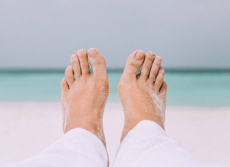 Male's legs on the white sand near the sea. Travel and vacation concept
