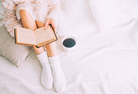 Young woman on the bed with old book and cup of coffee enjoys her stay.の写真素材