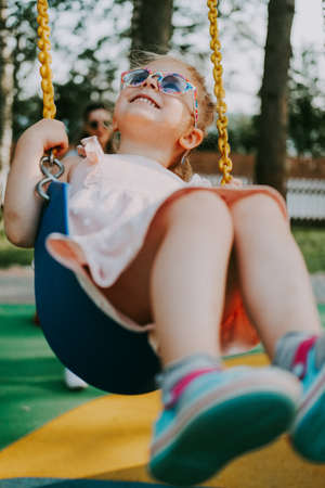 Happy Laughing child on swing in summer park. Girl in sunglasses have fun. Vintage film lookの写真素材