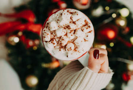Close up of women's hands holding white mug with hot cocoa, tea or coffee and marshmallow. Winter and Christmas time concept.の写真素材