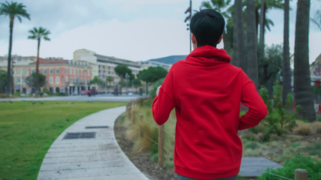 Female jogging in the city. Athletic girl wearing in red sports sweatshirt with long- sleeved. Girl runs outdoor listening music with earphones.の写真素材