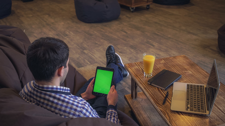 The man sits back in the hands holding the tablet, welcome companion, a green screen.の写真素材