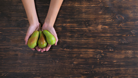 Unrecognizable woman holding fruits over the wooden table. Close up female hands with green pearsの写真素材