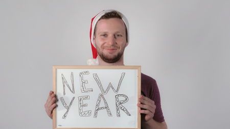 young caucasian man wearing santa hat for christmas holding whiteboard with handwriting words new year. Portrait handsome guy celebrating winter holidaysの写真素材