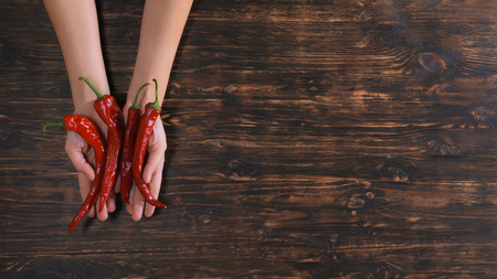 Unrecognizable woman holding vegetables over the wooden table. Close up female hands with chilliの写真素材