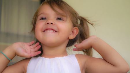 Portrait cute baby with blond hair. Cute little girl jumping and clap ones hands. Beautiful child 3-4 years old smiling.の写真素材