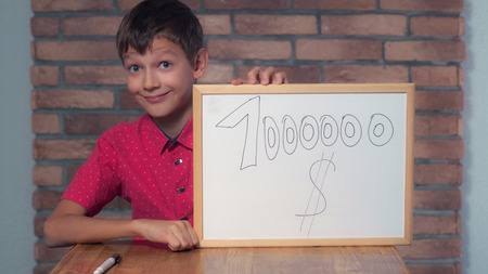 Portrait little boy showing whiteboard with handwriting word million dollars. Child put a signature. Preadolescent wearing in casual red shirt. Schoolboy with happy friendly smile.の写真素材