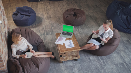 Informal business meeting two women negotiate. Consider charts make notes in the notebook. Laptop with green screen on the tableの写真素材
