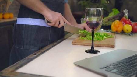 Close up details man cooking salad male hands cutting vegetables. On cook table wineglass and laptopの写真素材