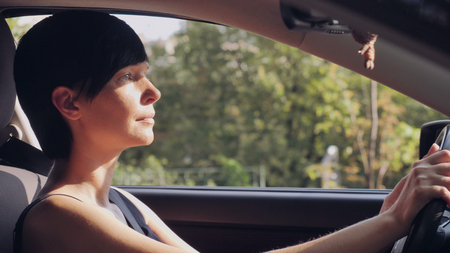 Adult brunette driving car. Caucasian woman sitting on drivers seat looking forward on the road.の写真素材