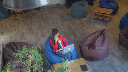 Businesswoman talking with partner using smartphone. Happy asian woman sitting in the modern contemporary loft with casual interior design. Worker answer call typing on the computer. On the wooden desk modern device.Top view.の写真素材