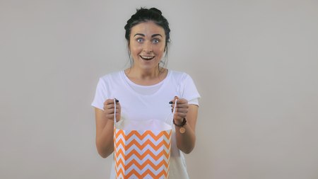 surprised caucasian woman with black hair looking into the package with happy smile Portrait young girl wearing casual white t-shirtの写真素材