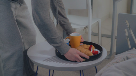 Closeup details man puts a tray with breakfast and engagement ring in red gift box on the coffee table near bed.の写真素材