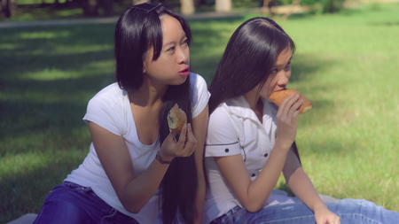 Portrait two asian woman eating bakery outdoors. Sisters talking and smiling.の写真素材