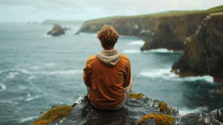 Photo concept of a man sitting on a rock by the seashore, gazing out at the sea with a contemplative and peaceful demeanor Generative AIの素材