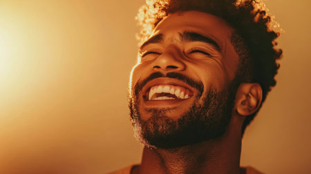 A man expresses pure joy, laughing heartily as warm golden light casts a glow on his face, highlighting his infectious smile indoors, showcasing a moment of genuine happiness.の素材