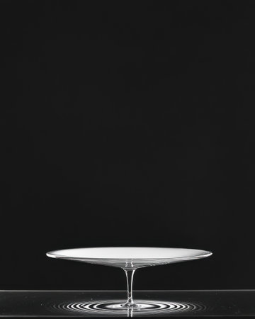 A delicate glass dish hovers gracefully above calm waters, creating ripples beneath it. The minimalist black-and-white tones emphasize the elegance and simplicity of the scene.の素材
