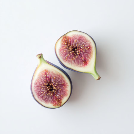A freshly picked fig is cut in half, revealing its rich purple exterior and intricate pink and white interior with tiny edible seeds, perfect for culinary presentation or healthy snacking.の素材