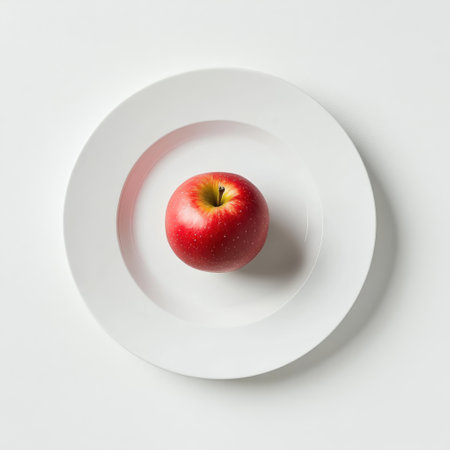 A single red apple is placed in the center of a simple white plate, showing its vibrant color against the clean background. This minimalistic setting emphasizes natural beauty.の素材