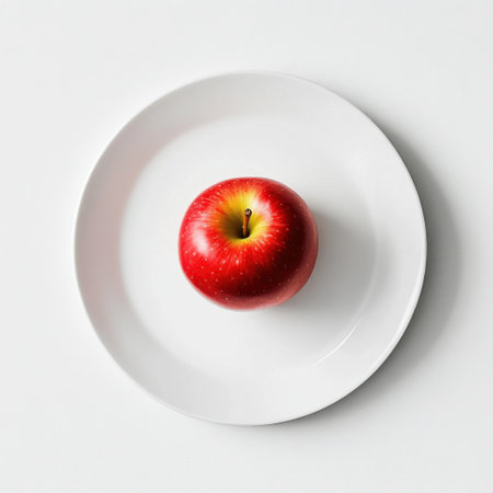 A vibrant red apple sits centered on a white plate placed on a minimalistic surface, showing its smooth skin and rich color, inviting a sense of freshness and simplicity.の素材
