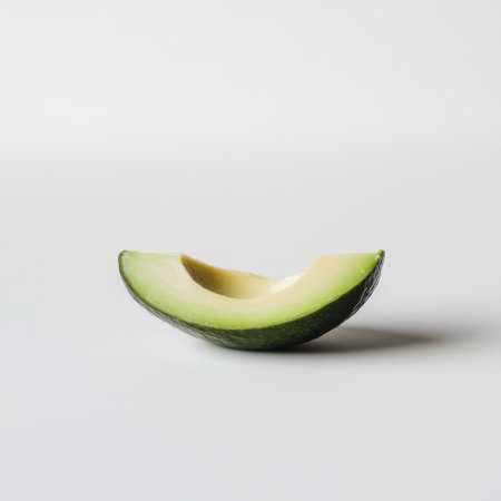 A ripe avocado slice, showing its creamy green interior and thin dark green skin, rests on a clean white surface, highlighting its freshness and natural beauty.の素材