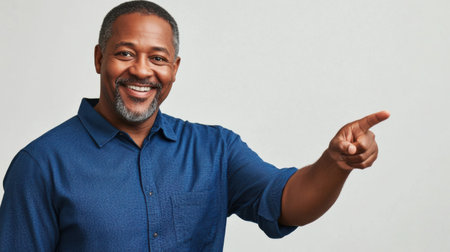 The image features a middle-aged man with dark skin and a goatee smiling while pointing. He stands in a well-lit studio with a neutral background, conveying positivity and engagement.の素材