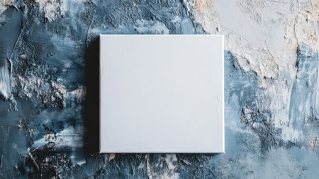 A minimalistic abstract canvas painted white features faint pencil marks. It is positioned against a textured surface that combines shades of blue and gray, creating a modern art aesthetic.の素材
