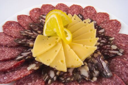 pieces of different types of sausage with hard cheese and lemon on a white plate