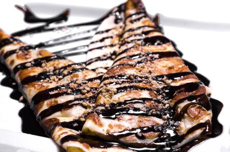 Pancakes with chocolate topping, nuts and sweet filling on a white plate