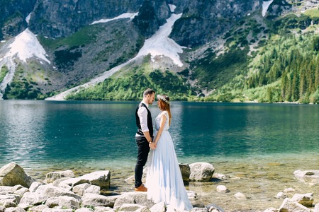 bride with the beautiful blue dress and groom hugging with views of the beautiful green mountains and lake with blue waterの写真素材