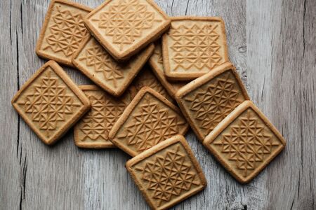 Square shortbread biscuits on the wooden background with ornament on it. Pile of cookies, warm home food photo photo,  layout. Quadrate cookies.の写真素材