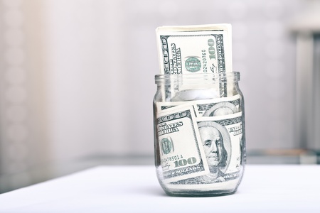 Many 100 US dollars bank notes in a glass jar in home interiorの写真素材