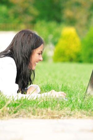 Caucasian college student lying down on the grass working on laptop at campus and laughing. Sunny day.の写真素材