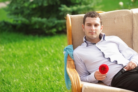 Thoughtful young man with flower looking at copyspace - Outdoors. Sunny day. Man is probably waiting for his girlfriend.の写真素材