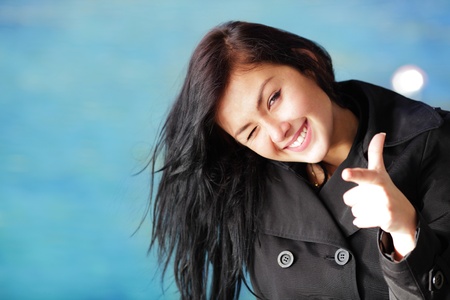 Young happy brunette woman on the beach winking and pointing at youの写真素材