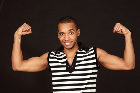 Young african-american muscular man in striped t-shirt on dark backgroundの写真素材