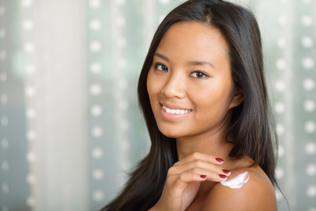 Portrait of a beautiful asian woman putting cream on her shoulderの写真素材