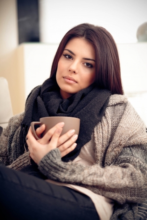 Young pensive woman in cozy warm clothings with cup of coffeeの写真素材