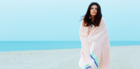 Young beautiful woman wrapped herself with blanket on the beachの写真素材